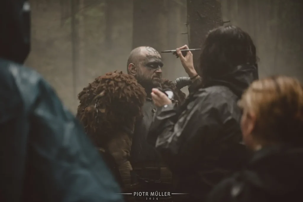 Charakteryzatorka malująca tatuaże na twarzy wojownika w kostiumie na planie filmu LARP