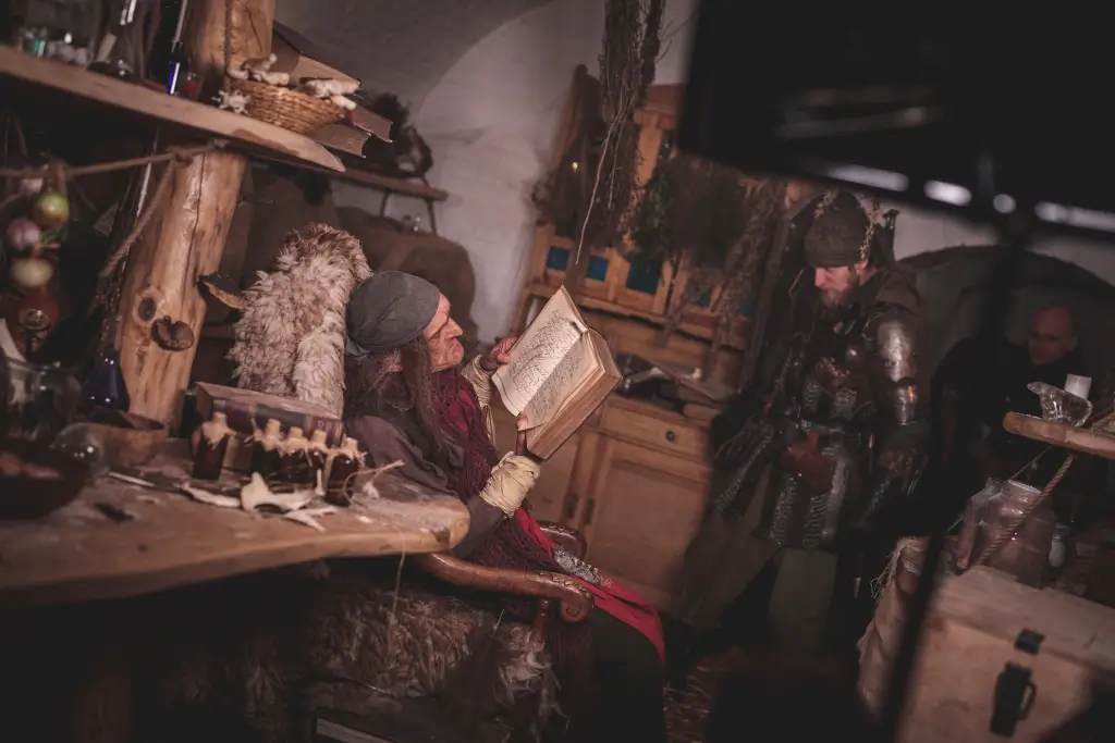 Wnętrze chatki guślarza – postać czyta księgę, klimat średniowieczny fantasy